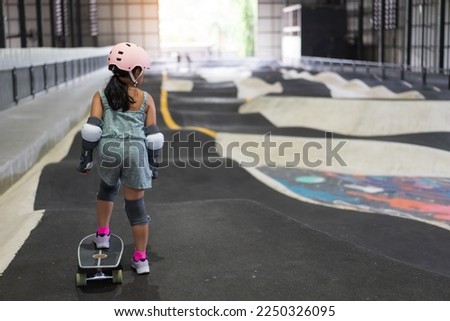 asian child skater or kid girl fun playing skateboard or start ride surf skate in indoor pump track skate park by extreme sports surfing to wearing helmet elbow pads wrist knee support for body safety Royalty-Free Stock Photo #2250326095