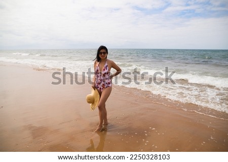 Beautiful young woman posing on the beach with a hat to protect herself from the sun. The woman is enjoying her trip to a paradise beach. Holiday and travel concept.