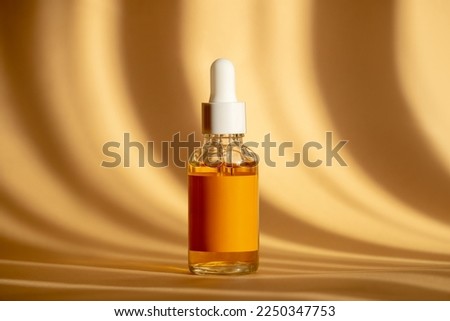 Glass bottle with white dropper lid with serum on brown background in sunlight. Orange essence in transparent unmarked container. Mockup of cosmetic product for skin care Royalty-Free Stock Photo #2250347753