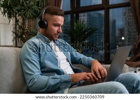 Serious handsome businessman wearing casual wear, headphones listening podcast sitting on sofa in background. Concept of considered business person, pondering man, information, internet communication