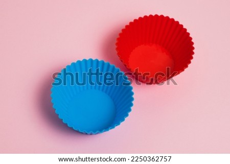 Red and blue silicone cupcake molds on a pink paper background.
