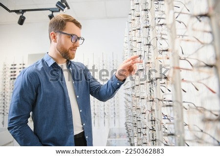 In Optics Shop. Portrait of male client holding and wearing different spectacles, choosing and trying on new glasses at optical store. Man picking frame for vision correction, closeup Royalty-Free Stock Photo #2250362883