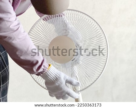 Gloved hand carrying an electric fan Royalty-Free Stock Photo #2250363173