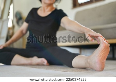 Healthy and happy 60s retired Asian woman in workout clothes stretching her leg, warming up, practicing yoga in her living room. cropped image Royalty-Free Stock Photo #2250374525
