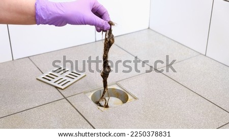 Water drain hole is clogged with hair clump. Woman hand in gloves is cleaning the bathroom sewer trap. Close-up. Clean shower sewerage. Bath plug hole blocked with dirt. Hair loss problems. Anti-odor. Royalty-Free Stock Photo #2250378831