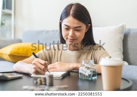 Saving money wealth concept, asian young business woman hand write management budget for saving cost, cash finance planning to spend enough money on her income for save money, payment tax, investing. Royalty-Free Stock Photo #2250381551