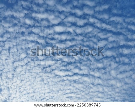 A mackerel sky is a common term for clouds made up of rows of Altocumulus rippling pattern similar in appearance to fish scales. Altocumulus floccus white fluffy clouds covering the blue sky.  Royalty-Free Stock Photo #2250389745