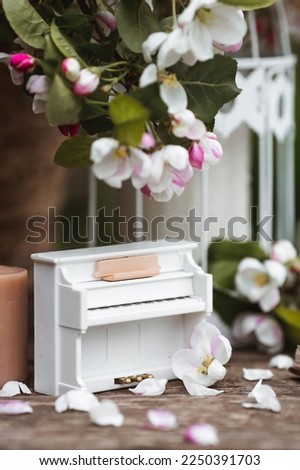 A beautiful postcard. A white piano, a statuette, candles, a book and a vase with a bouquet of blooming apple trees. A beautiful still life. The concept of classical music, poetry.