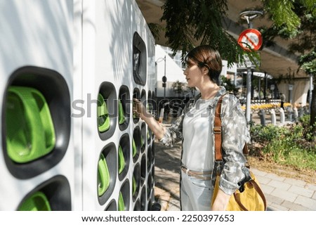 pretty Asian woman swapping portable batteries at the Battery charging exchange station. Taiwanese lady hand on battery handle Royalty-Free Stock Photo #2250397653