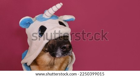 Creative funny dog in kigurumi pajamas. Concept pets look like person. Close-up portrait. Horizontal web banner with copy space. German Shepherd wears unicorn costume and sits on pink background.