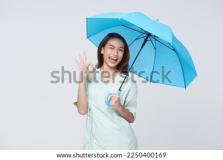 Happy Asian woman standing holding blue umbrella and showing ok sign isolated on white background, life insurance and protection concept.