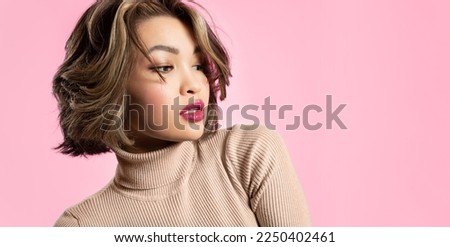 Beautiful Asian young woman with glowing skin, short haircut and red lips wearing stylish clothes on a pastel pink background Royalty-Free Stock Photo #2250402461