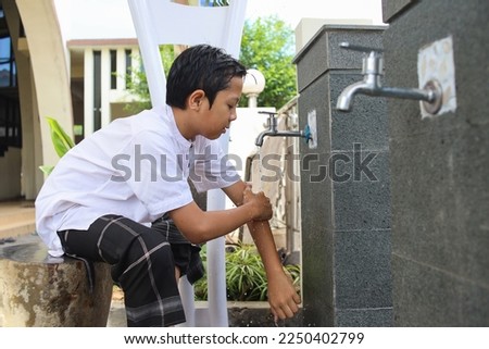 Muslim kid washing hands from hands to elbow, procedure of ablution before pray salah at the mosque Royalty-Free Stock Photo #2250402799