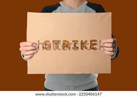 Woman holding Strike sign on dark orange background, closeup