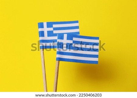 Small paper flags of Greece on yellow background, closeup