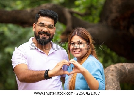Young indian couple making heart shape with hand at park.