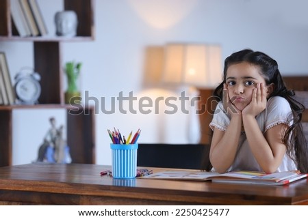 Portrait of an innocent child girl sitting on a chair with sad facial expression - studio, isolated . Stock image of a cute Indian girl sitting on a chair in the living room - holding her face 