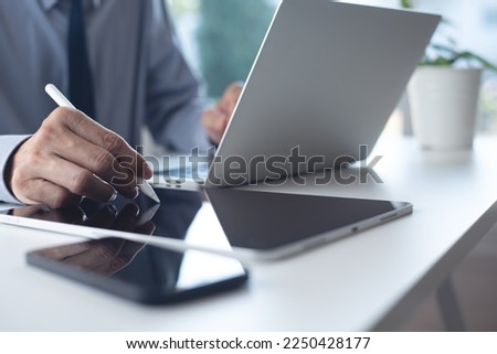 Close up of businessman hand using stylus pen signing e-document on digital tablet via mobile app and working on laptop computer on white office table, e-signing, electronic signature concept Royalty-Free Stock Photo #2250428177