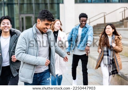 Multiracial friends running and enjoying time together at city or university - Happy friendship and diversity concepts with millennial young people living a carefree lifestyle Royalty-Free Stock Photo #2250447903