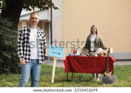 Man with sign Yard sale and woman near table of different items outdoors