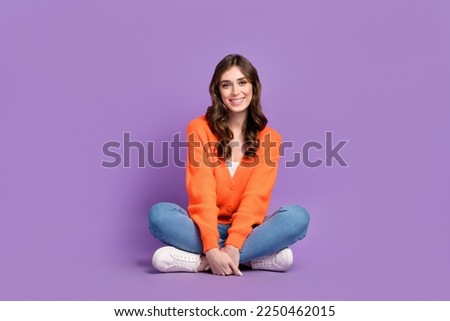Full length photo of charming adorable woman dressed orange sitting floor legs crossed isolated purple color background