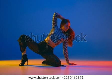 Passion. Portrait of young girl dancing high heel dance in stylish clothes over blue background in neon light. Concept of dance lifestyle, modern style, contemporary, youth culture, self-expression Royalty-Free Stock Photo #2250462871