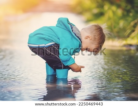 Cute little child standing in the puddle and playing with rainwater. Toddler walking in nature after rain. Royalty-Free Stock Photo #2250469443