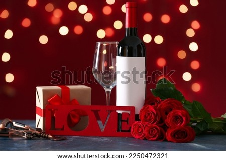 Bottle of wine, rose flowers, gift and text LOVE on black table against blurred lights. Valentine's Day celebration
