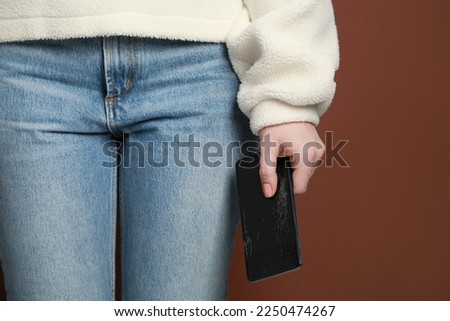 Woman holding damaged smartphone on brown background, closeup. Device repairing