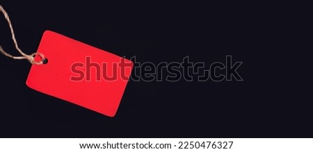 An empty red price tag with a place to insert text on a string on a black background. Copy space