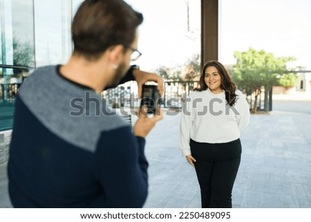 Beautiful latin fat woman taking pictures for her social media content with the help of a caucasian man 
