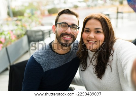 Personal perspective of a handsome caucasian boyfriend and fat girlfriend looking happy taking a selfie together at a restaurant