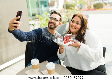 Attractive influencer fat woman and smiling man taking a selfie for their social media content while eating cake and drinking coffee 