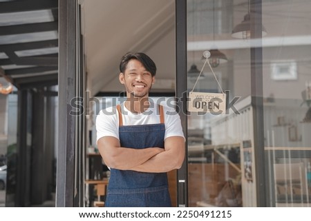 Young Asia coffee shop owner business man in apron with open sign at door shop.
