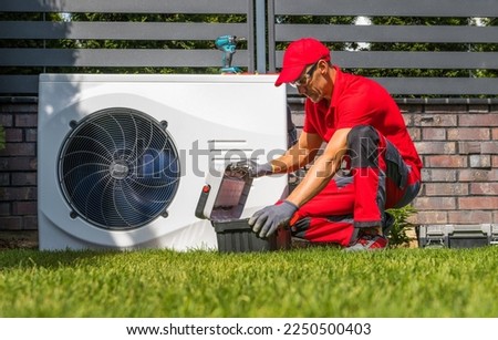 Professional Caucasian Heat Pumps Technician in His 40s Installing New Residential Modern Heating Device. HVAC Industry Theme. Royalty-Free Stock Photo #2250500403