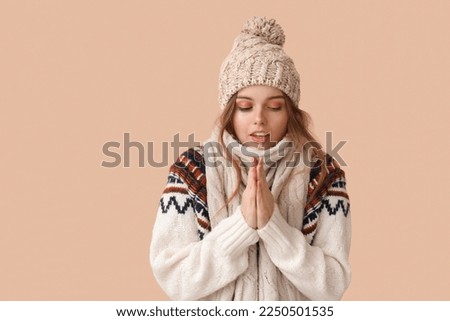 Frozen young woman in winter clothes on beige background