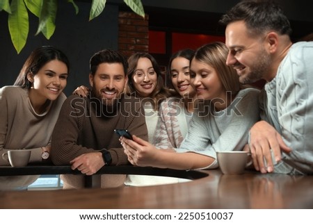 Young woman showing something funny at smartphone to her friends in cafe