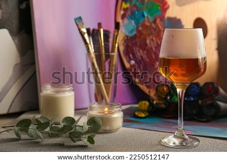 Brushes with colorful paints, candles and glass of wine on light gray table