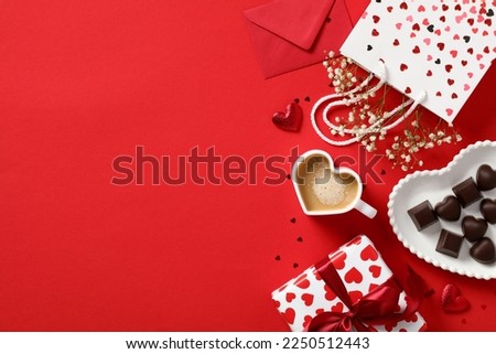 Romantic Valentine's Day concept. Top view Love letter, heart-shaped coffee cup, candies, and gift box on red background.