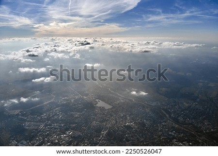 Aerial view from airplane window at high altitude of distant city covered with layer of thin misty smog and distant clouds. Royalty-Free Stock Photo #2250526047