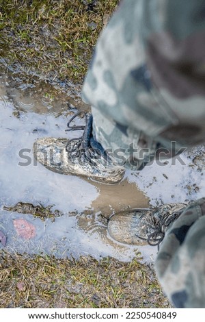 Close-up for a man's legs in military camouflage with a trekking wellington shoes dirty in mud.
