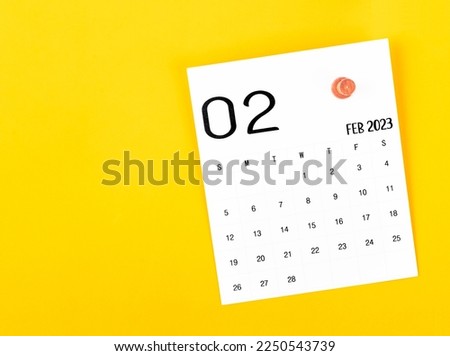 February 2023 calendar and wooden push pin on yellow background.
