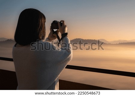 Young Asian woman take a photo at beautiful sunrise and colorful sky in the mist over the mountain