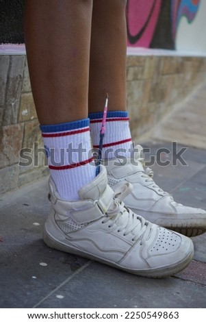 paintbrush, woman in colorful socks in white sneakers with paintbrush on her feet