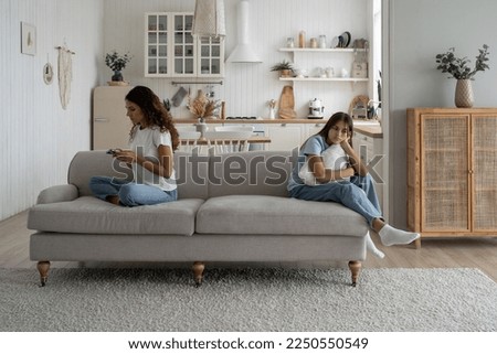 Focused busy woman mother using smartphone during family time child daughter at home. Working from home mom looking and mobile phone screen, ignoring sad upset teen girl kid. Parents and screen time