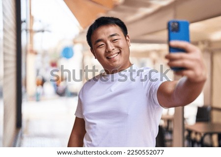 Young chinese man smiling confident making selfie by the smartphone at street