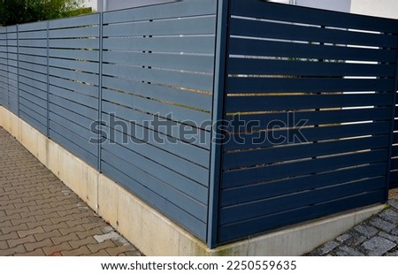 metal fillings of fence with an underlay of concrete blocks. A metal aluminum fence will provide privacy around the garden. horizontal slats cover well. a hedge made of tuji adds protection, concrete Royalty-Free Stock Photo #2250559635