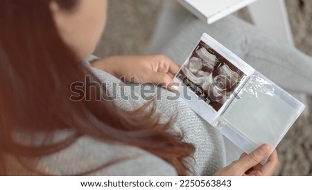 Pregnant woman holding and looking sonogram or ultrasonography picture of her unborn baby.