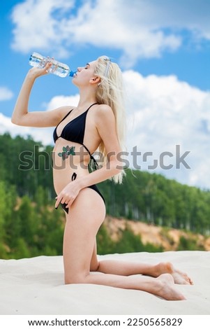 Portrait of a young beautiful blonde girl in black bikini posing on a sand pit background