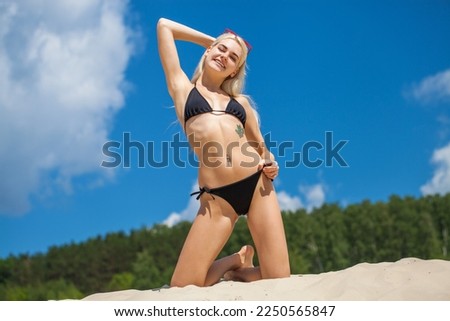 Portrait of a young beautiful blonde girl in black bikini posing on a sand pit background